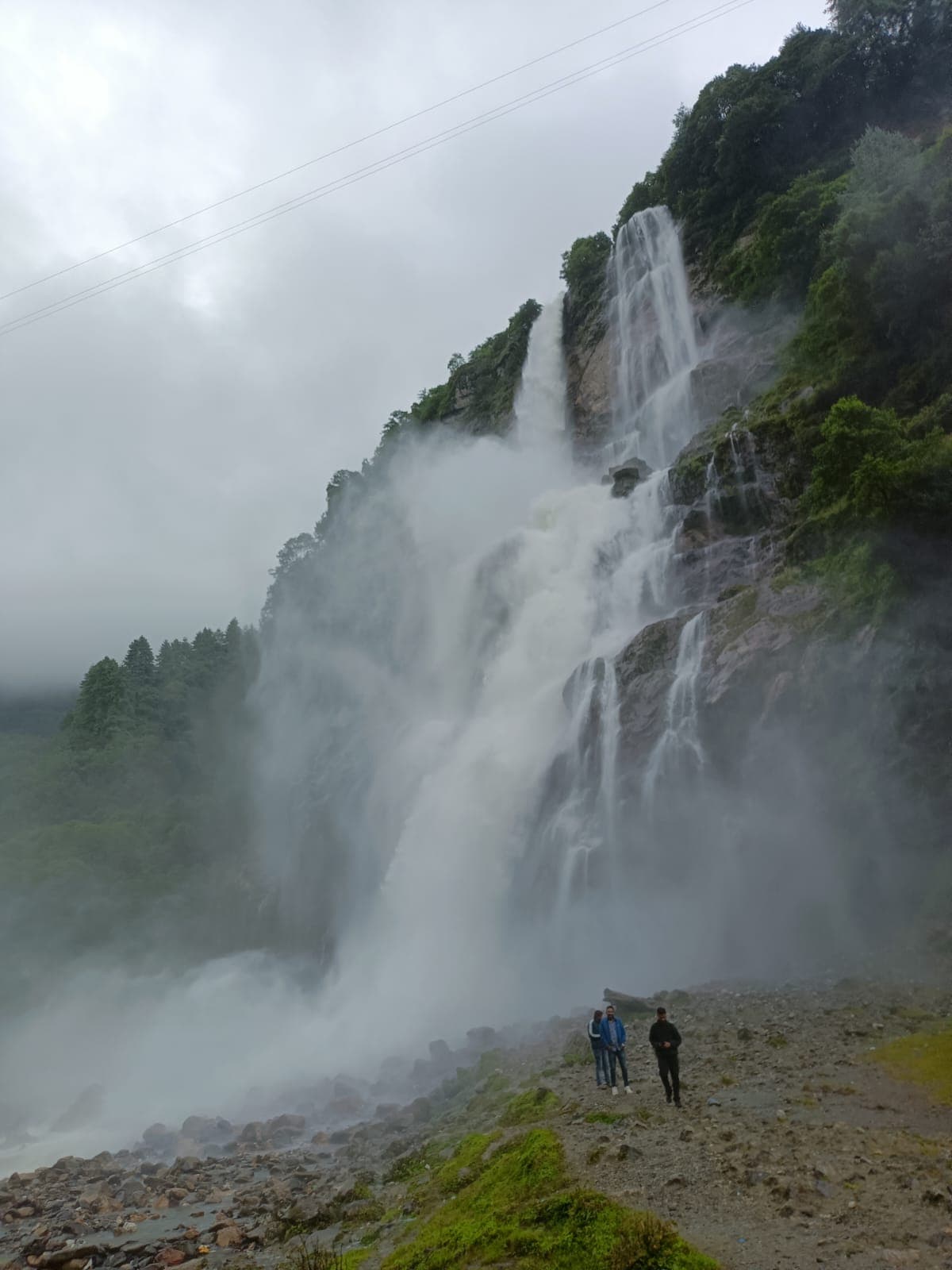 Visitors standing near a wide waterfall shrouded in spray