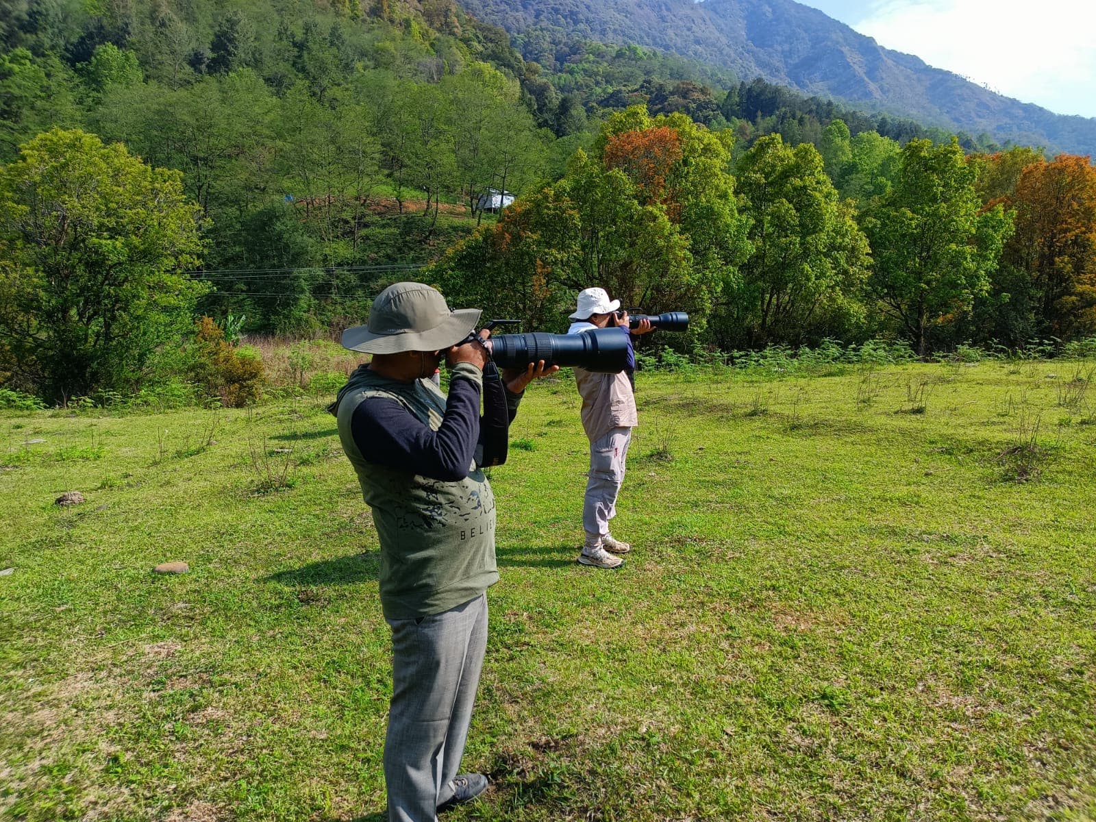 Visitors photographing a green meadow beneath forested hills
